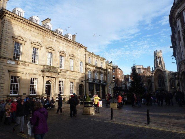 A street shot of St Helen's Square, York. Showing pedestrians, a georgian house and in the distance, St Helen's Church, on a sunny day.