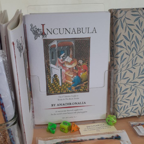 a 5e RPG adventure setting book based on book history, titled Incunabula, resting on a shelf along with some dice.
